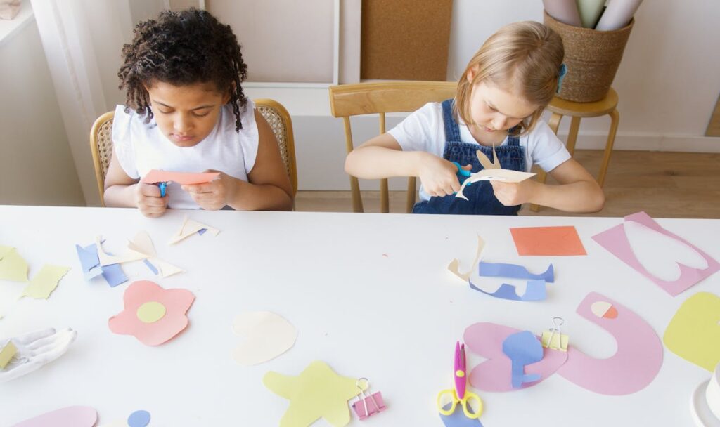 Two children crafting colorful paper shapes, focusing on creativity and fun in an indoor setting.