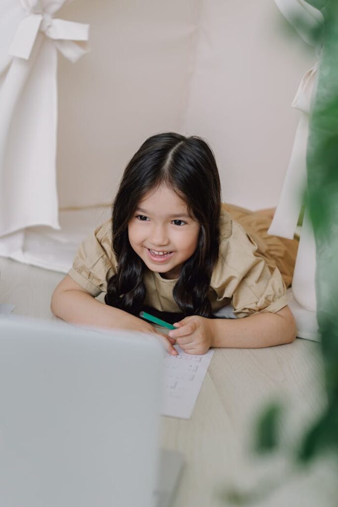 Cute Asian girl smiling while using a laptop for her online class, showcasing joyful learning.