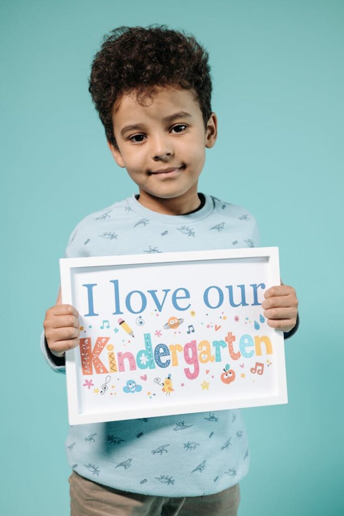 Cheerful child holding a colorful kindergarten sign against a blue backdrop.