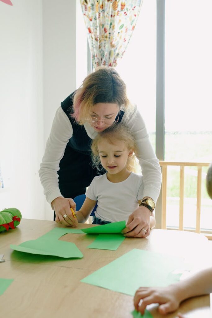 A teacher assists a young girl with a craft project in a classroom setting.