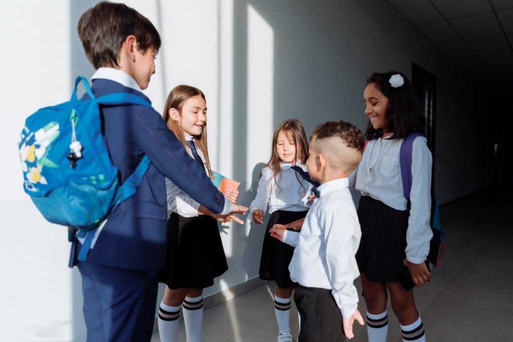 Group of children in school uniforms playing rock paper scissors indoors.